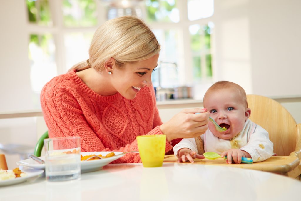 Mom feeding baby in highchair at the family table